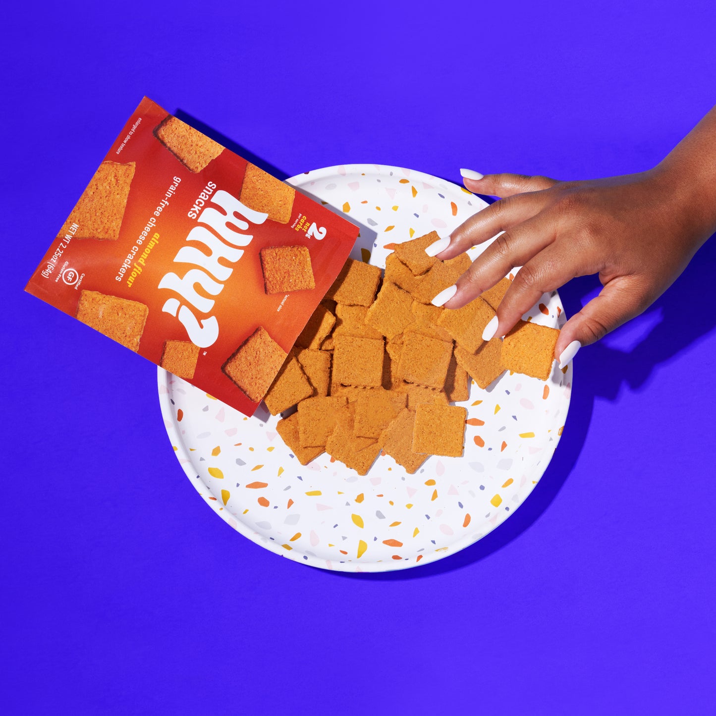 Woman's hand grabbing a cheese cracker off of a plate.